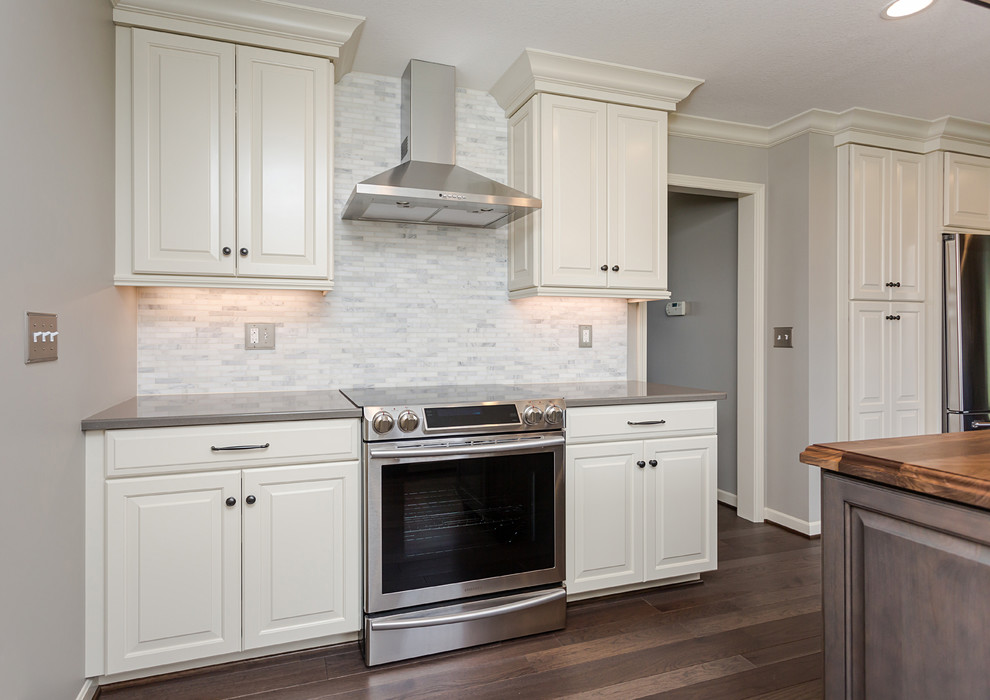 Example of a mid-sized farmhouse u-shaped medium tone wood floor and brown floor eat-in kitchen design in Other with a farmhouse sink, raised-panel cabinets, white cabinets, quartz countertops, multicolored backsplash, marble backsplash, stainless steel appliances and an island