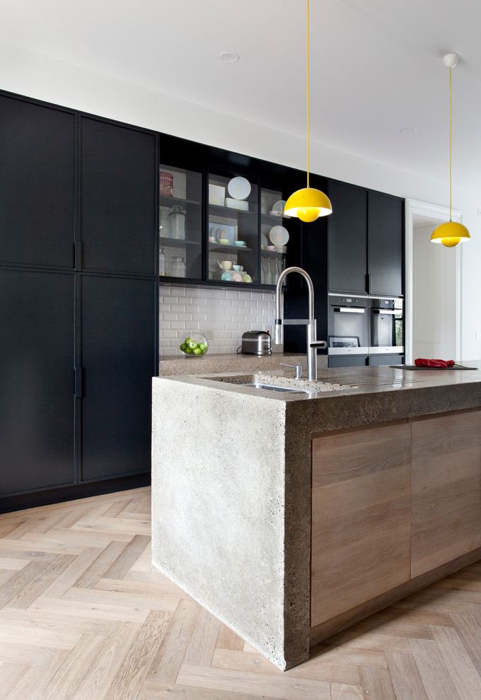 Kitchen - contemporary galley light wood floor kitchen idea in Dublin with flat-panel cabinets, black cabinets, concrete countertops and an island