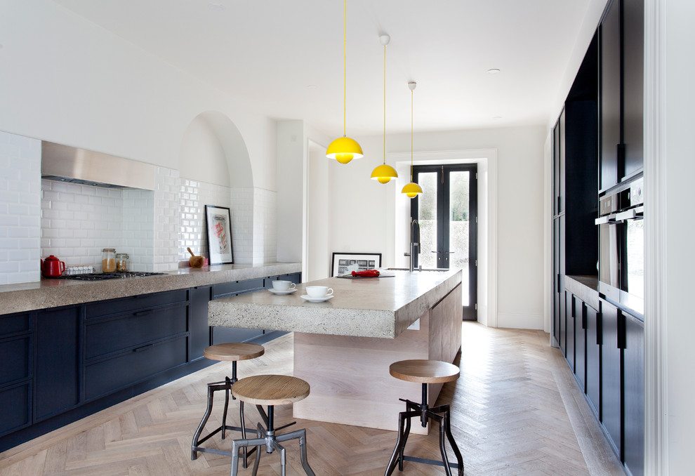 Zweizeilige Moderne Küche mit flächenbündigen Schrankfronten, schwarzen Schränken, Betonarbeitsplatte, hellem Holzboden und Kücheninsel in Dublin