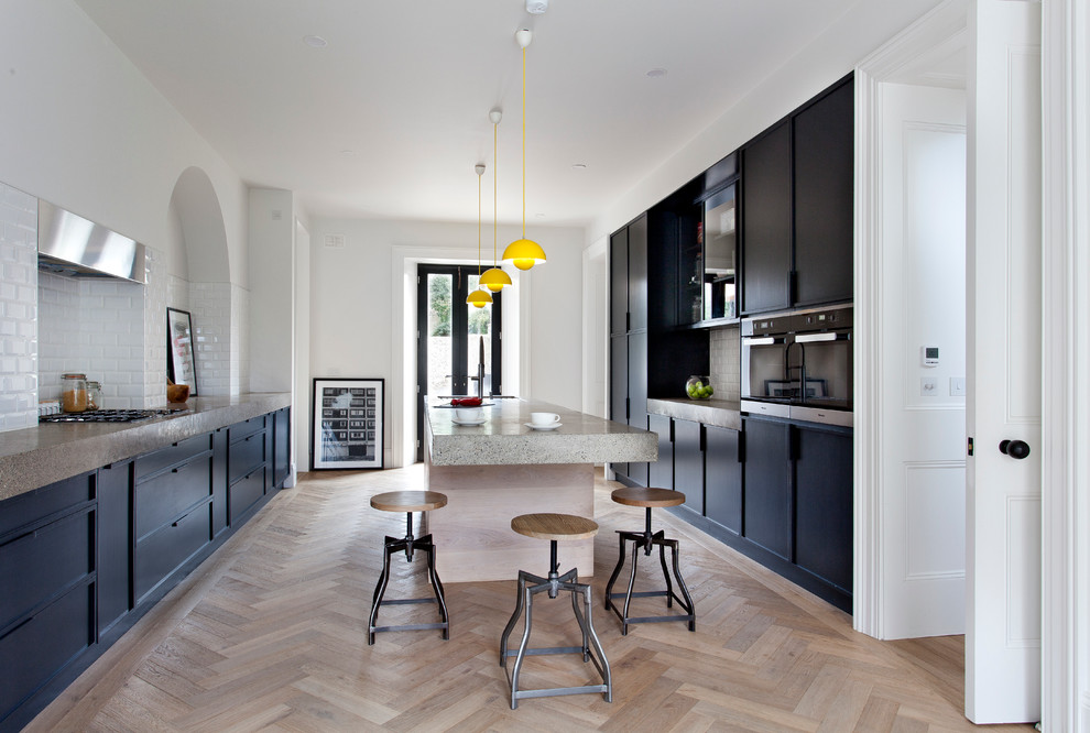 Exemple d'une cuisine parallèle tendance avec un placard à porte plane, des portes de placard noires, un plan de travail en béton, parquet clair et îlot.
