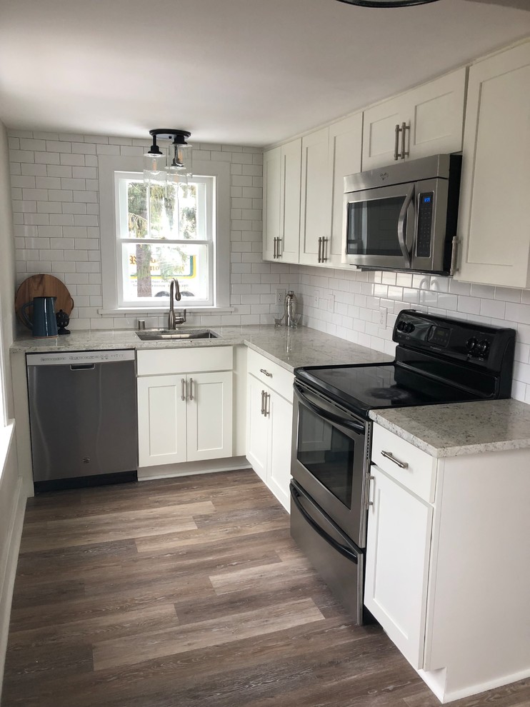 This is an example of a small farmhouse l-shaped enclosed kitchen in Milwaukee with a submerged sink, shaker cabinets, white cabinets, granite worktops, white splashback, ceramic splashback, stainless steel appliances, vinyl flooring, no island, brown floors and white worktops.