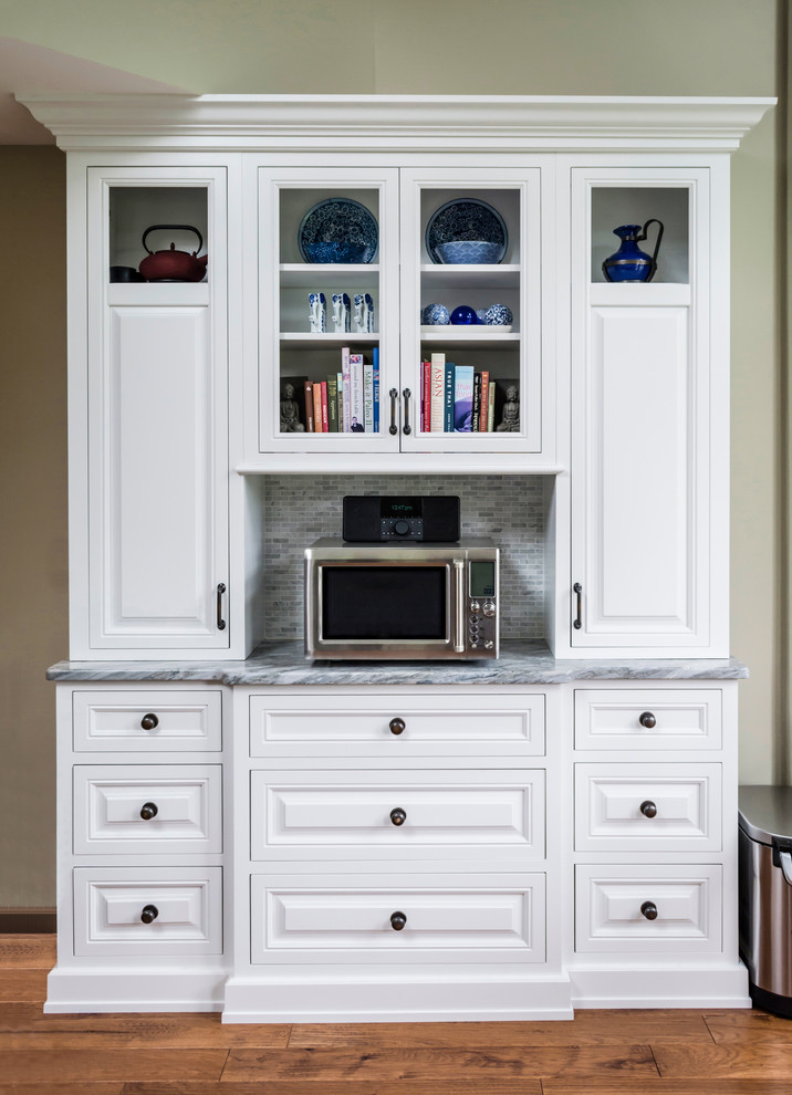 Klassisk inredning av ett mellanstort l-kök, med en rustik diskho, luckor med upphöjd panel, vita skåp, marmorbänkskiva, vitt stänkskydd, stänkskydd i stenkakel, rostfria vitvaror, mellanmörkt trägolv och en köksö