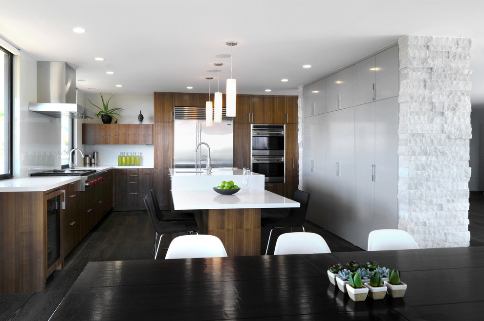 Large minimalist dark wood floor and brown floor eat-in kitchen photo in Los Angeles with a farmhouse sink, flat-panel cabinets, brown cabinets, quartz countertops, white backsplash, glass sheet backsplash, stainless steel appliances, an island and white countertops