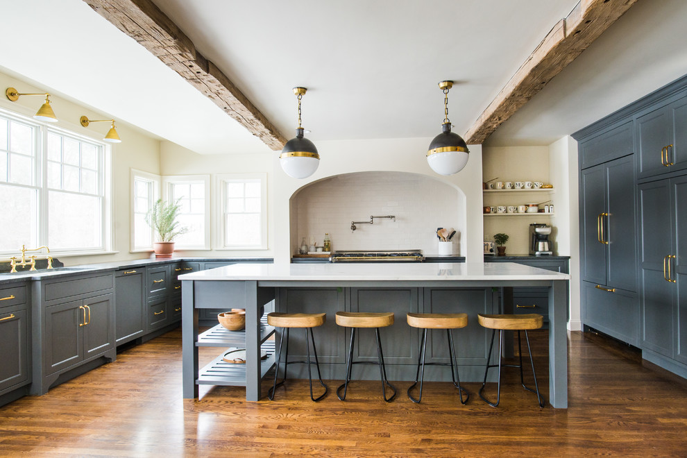 Photo of a farmhouse u-shaped kitchen/diner in Boston with a submerged sink, shaker cabinets, grey cabinets, white splashback, integrated appliances, medium hardwood flooring, an island, brown floors and white worktops.