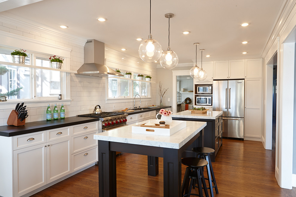 Example of a classic l-shaped medium tone wood floor kitchen design in San Francisco with an undermount sink, shaker cabinets, white backsplash, subway tile backsplash, stainless steel appliances and two islands
