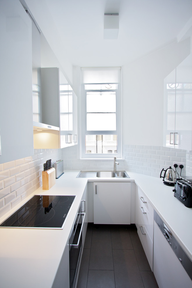 Enclosed kitchen - mid-sized contemporary u-shaped ceramic tile enclosed kitchen idea in London with a double-bowl sink, flat-panel cabinets, laminate countertops, white backsplash, ceramic backsplash, no island and paneled appliances