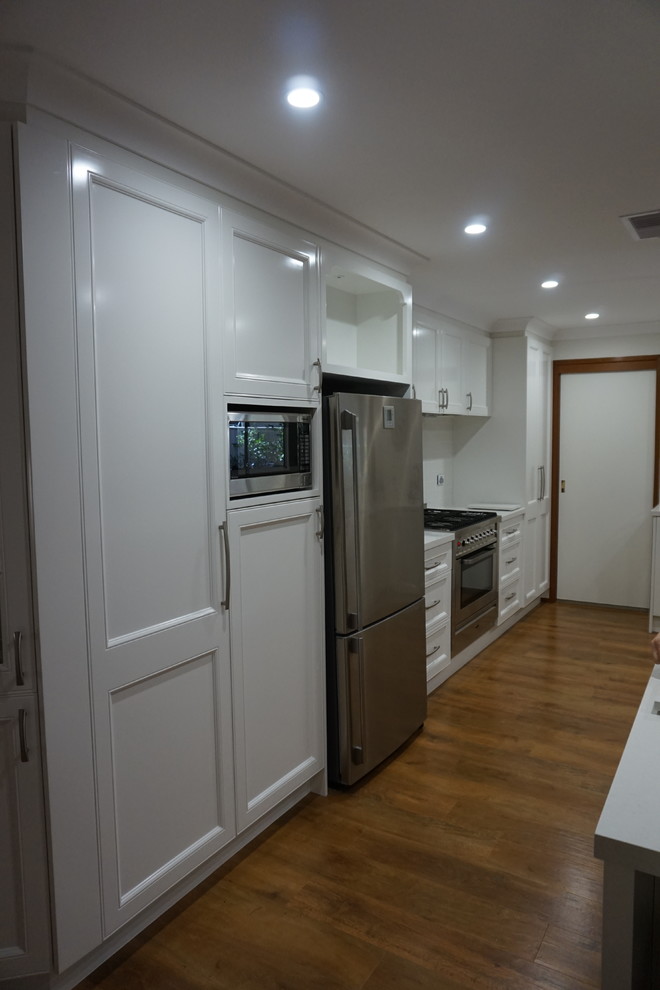 Exempel på ett modernt kök och matrum, med en nedsänkt diskho, luckor med infälld panel, vita skåp, bänkskiva i kvarts, vitt stänkskydd, stänkskydd i porslinskakel, rostfria vitvaror, ljust trägolv och en köksö