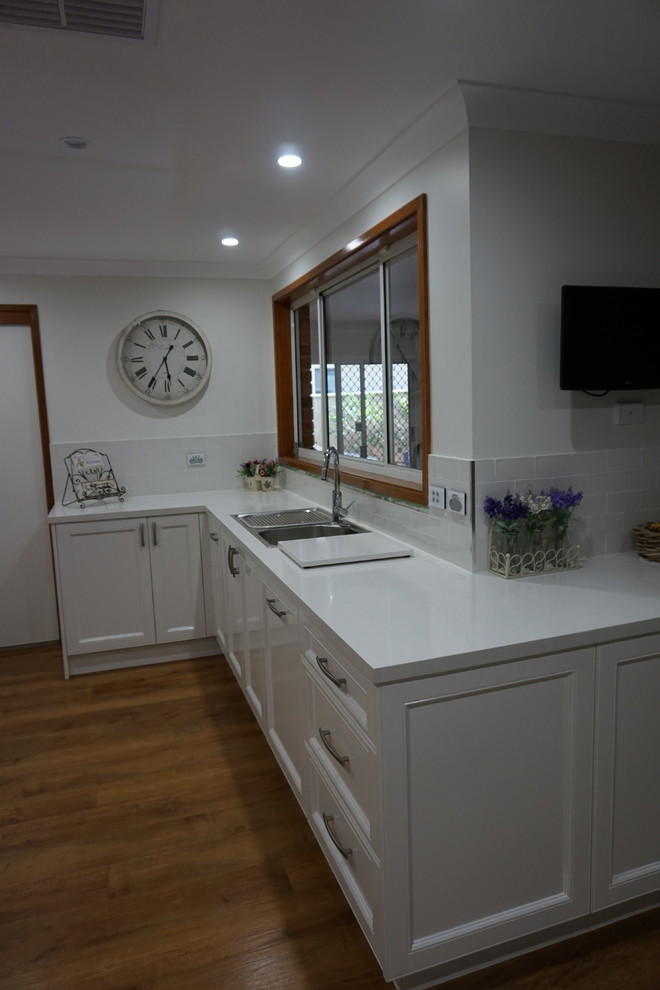 Exempel på ett modernt kök och matrum, med en nedsänkt diskho, luckor med infälld panel, vita skåp, bänkskiva i kvarts, vitt stänkskydd, stänkskydd i porslinskakel, rostfria vitvaror, ljust trägolv och en köksö