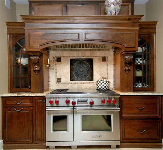 Modelo de cocina comedor tradicional con puertas de armario de madera oscura, encimera de granito, salpicadero beige, salpicadero de azulejos de piedra, electrodomésticos de acero inoxidable y una isla