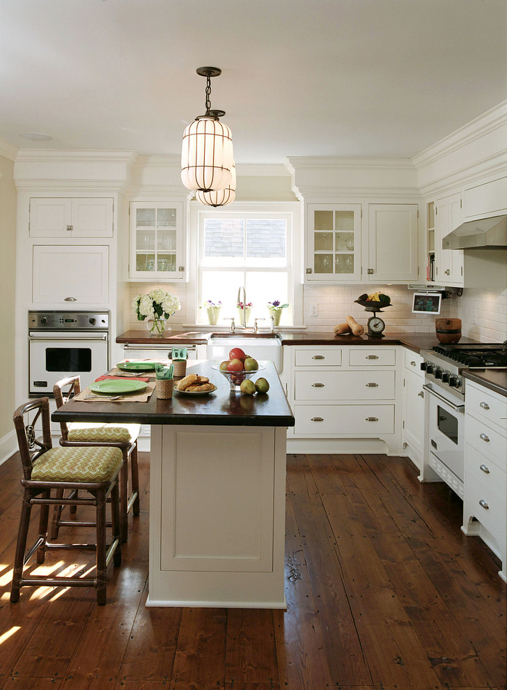 ニューヨークにあるトラディショナルスタイルのおしゃれなキッチン (エプロンフロントシンク、フラットパネル扉のキャビネット、白いキャビネット、白いキッチンパネル、サブウェイタイルのキッチンパネル、白い調理設備、濃色無垢フローリング) の写真