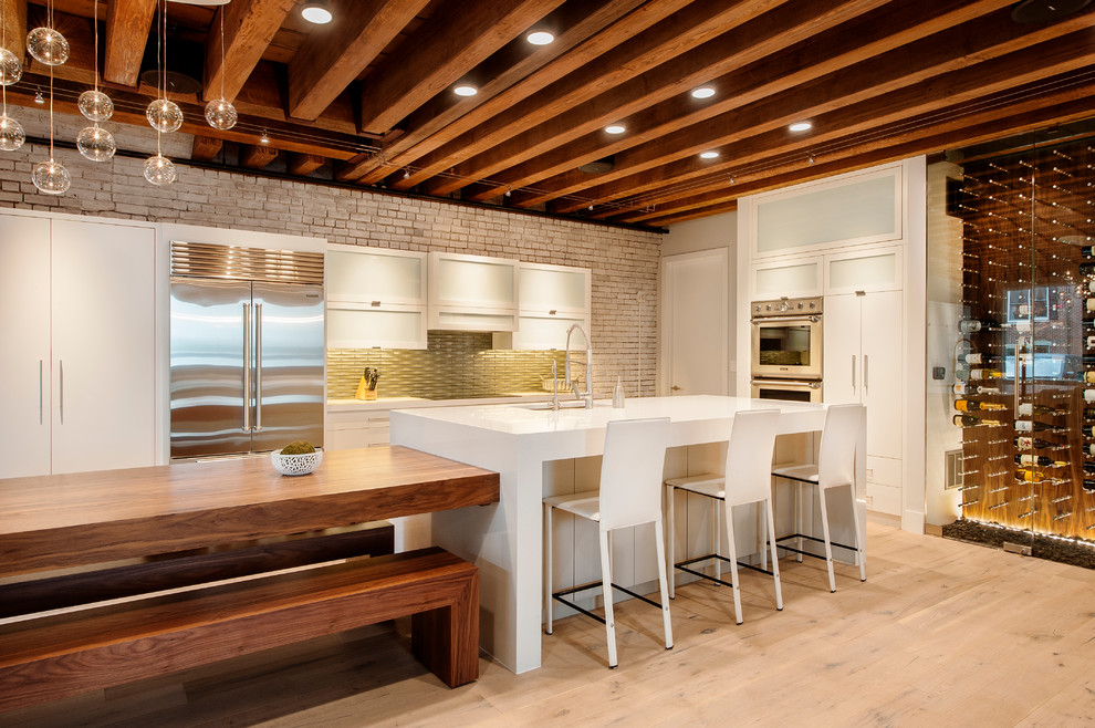 Large urban l-shaped kitchen/diner in Boston with flat-panel cabinets, white cabinets, grey splashback, stainless steel appliances, light hardwood flooring and an island.