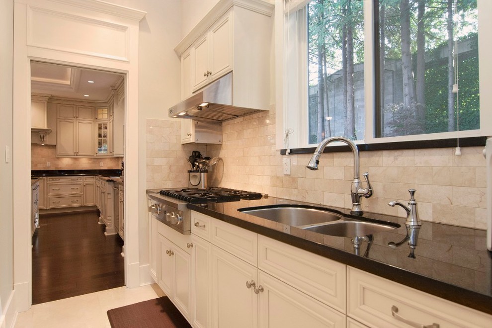 Elegant u-shaped eat-in kitchen photo in Vancouver with an undermount sink, raised-panel cabinets, white cabinets, granite countertops, beige backsplash and stainless steel appliances