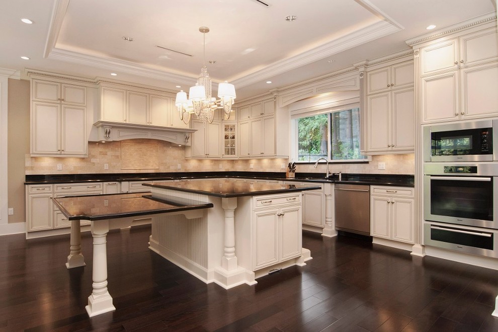 Example of a classic u-shaped eat-in kitchen design in Vancouver with an undermount sink, raised-panel cabinets, white cabinets, granite countertops, beige backsplash and stainless steel appliances