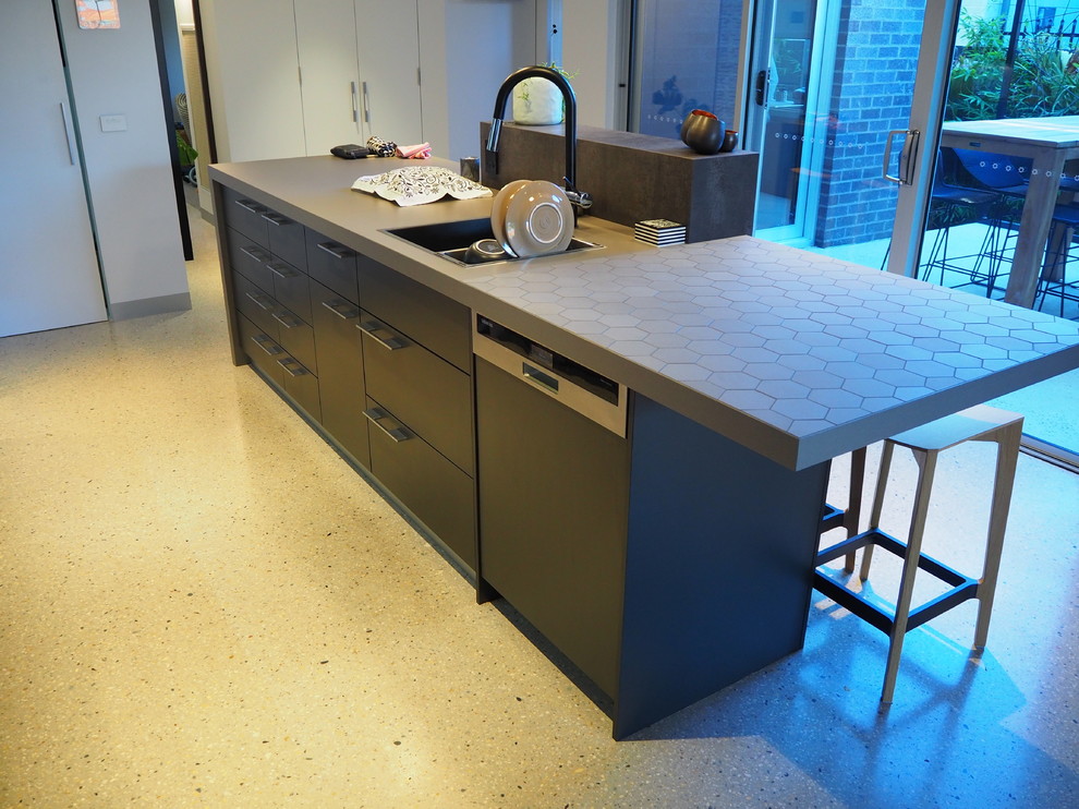 Exempel på ett mellanstort modernt kök, med en dubbel diskho, skåp i ljust trä, kaklad bänkskiva, blått stänkskydd, glaspanel som stänkskydd, svarta vitvaror, betonggolv och en köksö