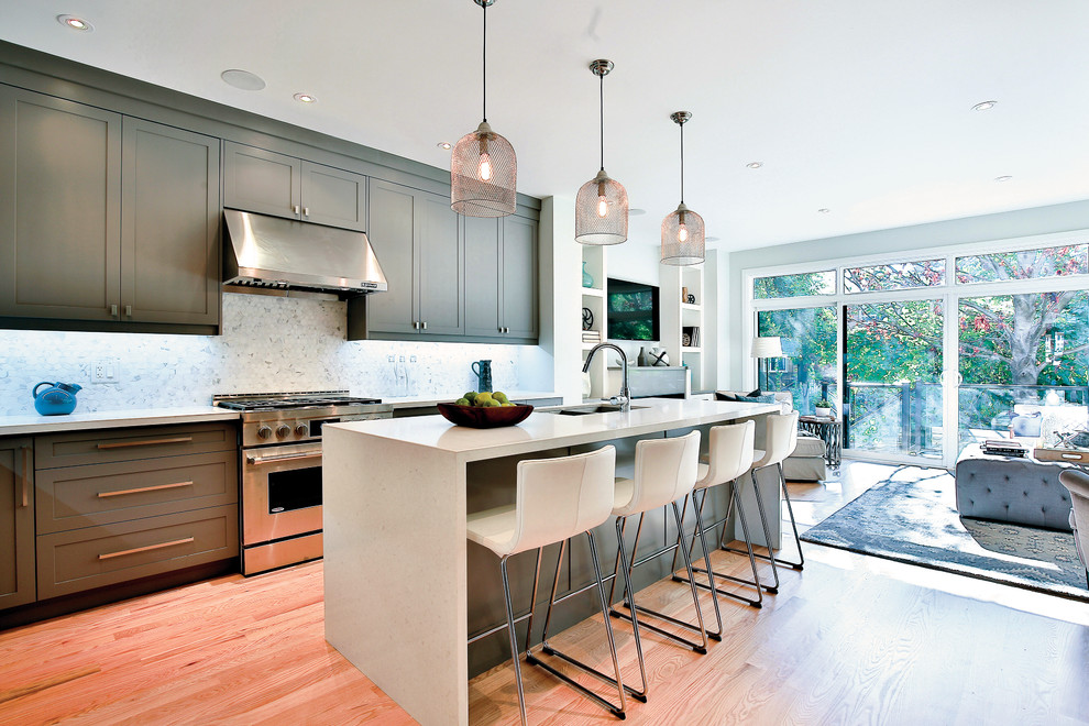 Mid-sized transitional l-shaped light wood floor open concept kitchen photo in Toronto with raised-panel cabinets, dark wood cabinets, marble countertops, gray backsplash, porcelain backsplash, stainless steel appliances and an island