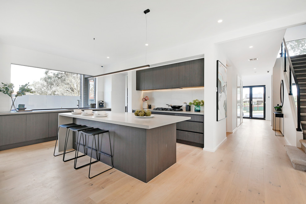 Trendy l-shaped light wood floor and beige floor kitchen photo in Melbourne with flat-panel cabinets, gray cabinets, an island and white countertops