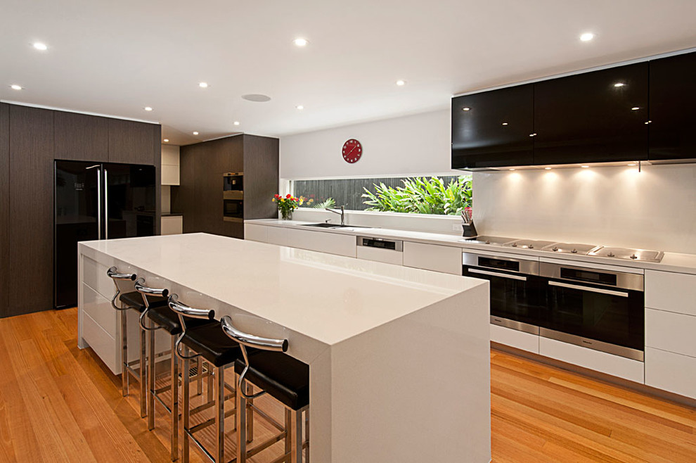 Zweizeilige Moderne Küche mit Vorratsschrank, Unterbauwaschbecken, flächenbündigen Schrankfronten, weißen Schränken, Quarzwerkstein-Arbeitsplatte, Küchenrückwand in Weiß, schwarzen Elektrogeräten, hellem Holzboden und Kücheninsel in Melbourne