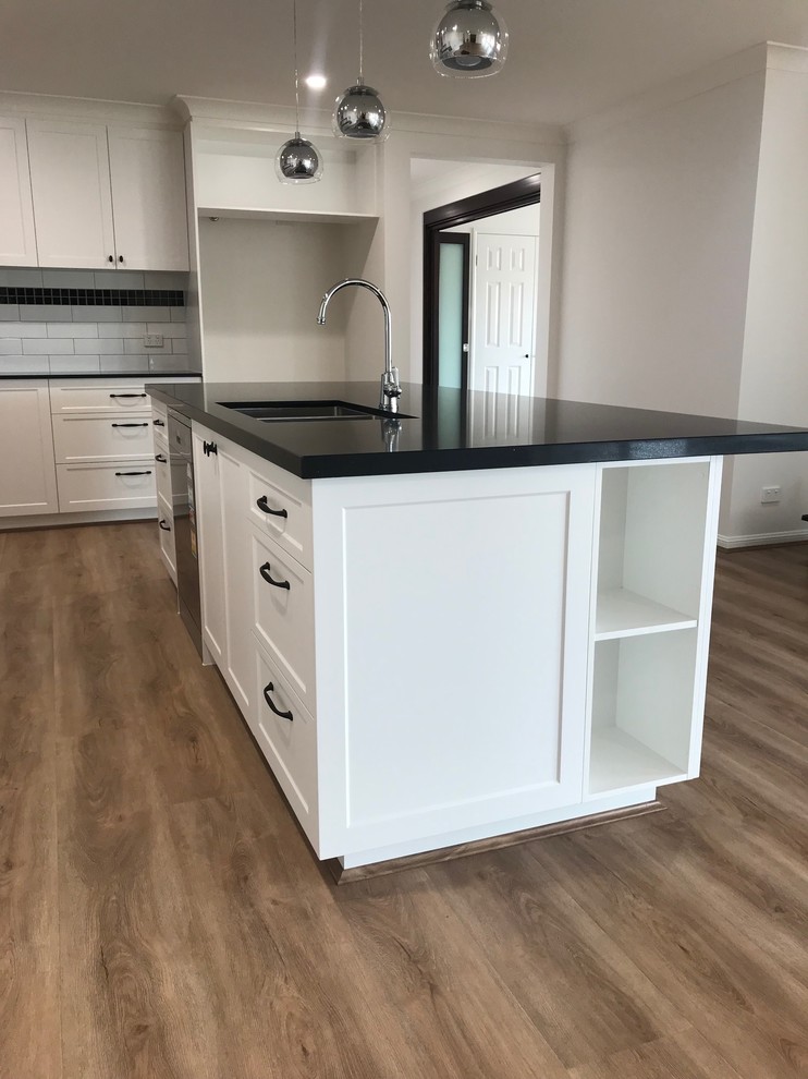 Large modern l-shaped kitchen/diner in Gold Coast - Tweed with a submerged sink, shaker cabinets, white cabinets, engineered stone countertops, multi-coloured splashback, porcelain splashback, coloured appliances, an island, brown floors and black worktops.