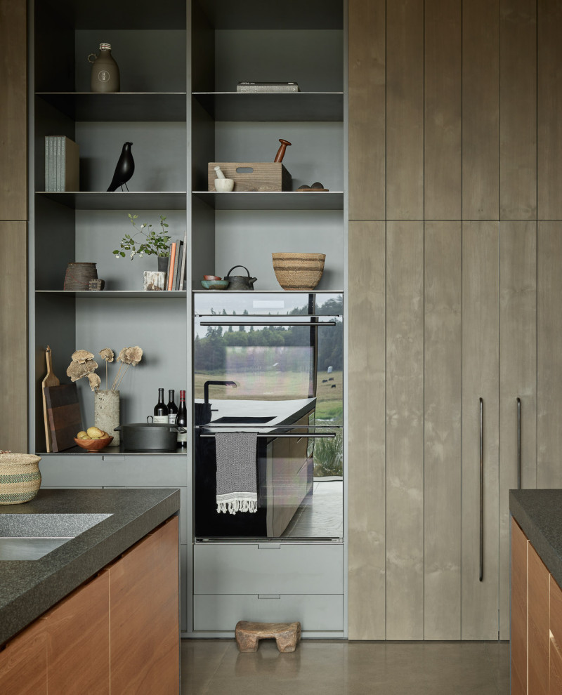 Ejemplo de cocina moderna grande con armarios con paneles lisos, encimera de granito, suelo de cemento, dos o más islas, encimeras negras y madera