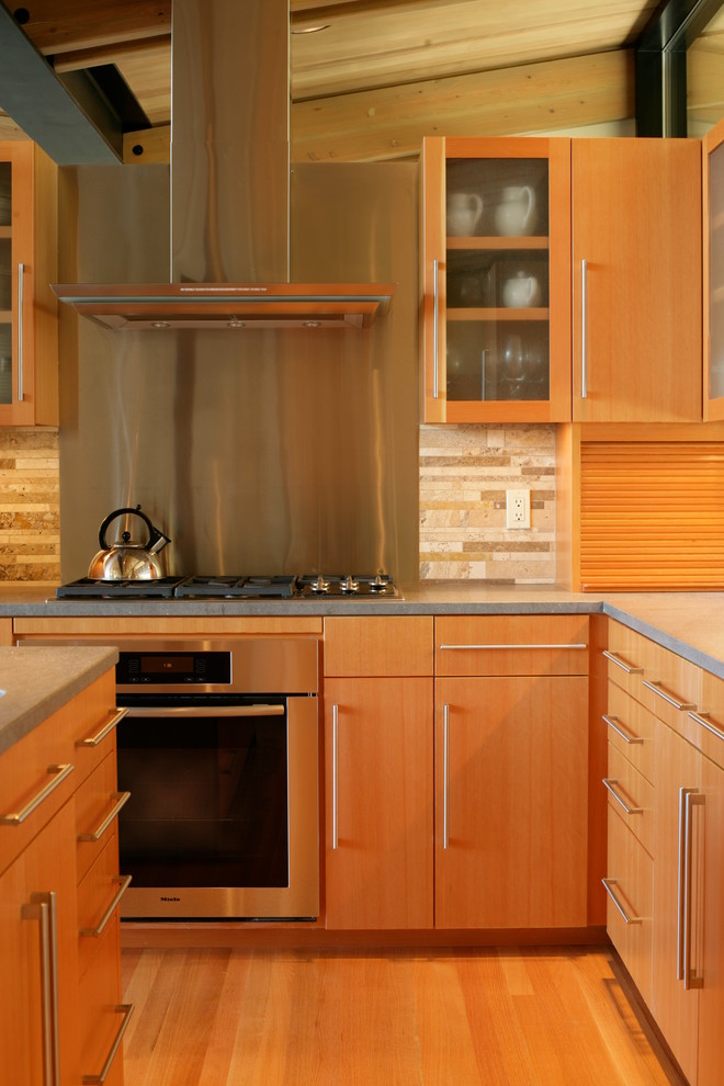 Bild på ett funkis kök, med släta luckor, skåp i ljust trä, bänkskiva i betong, stänkskydd i stenkakel, rostfria vitvaror, ljust trägolv och en köksö