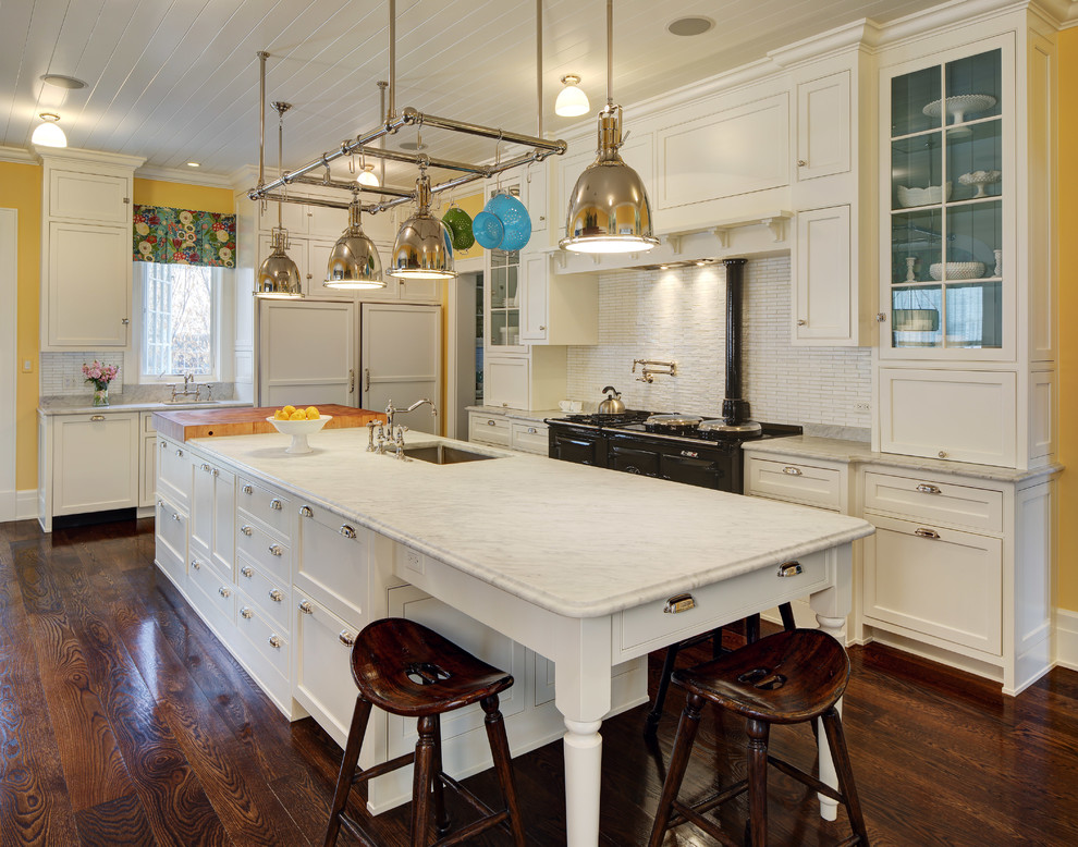 This is an example of a traditional l-shaped kitchen in Chicago with a submerged sink, shaker cabinets, white cabinets, white splashback, black appliances, dark hardwood flooring and an island.