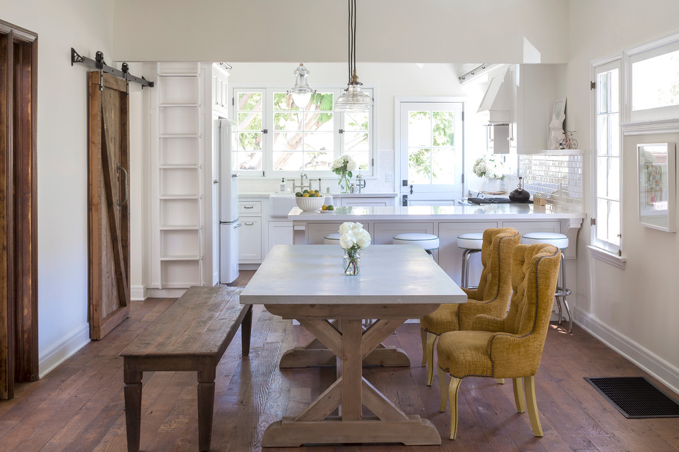 Mid-sized country u-shaped medium tone wood floor eat-in kitchen photo in Los Angeles with a farmhouse sink, shaker cabinets, white cabinets, solid surface countertops, white backsplash, subway tile backsplash, stainless steel appliances and a peninsula