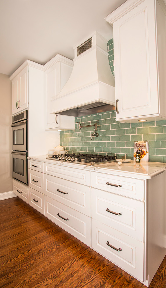 Bild på ett stort vintage kök, med en dubbel diskho, luckor med upphöjd panel, vita skåp, bänkskiva i kvarts, blått stänkskydd, stänkskydd i keramik, rostfria vitvaror, mellanmörkt trägolv och en köksö