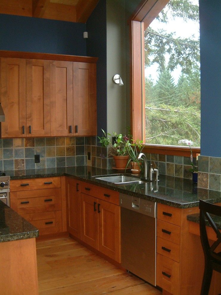 Inspiration pour une cuisine américaine minimaliste en L et bois brun avec un évier encastré, un placard à porte shaker, un plan de travail en granite, une crédence bleue, une crédence en carrelage de pierre et un électroménager en acier inoxydable.