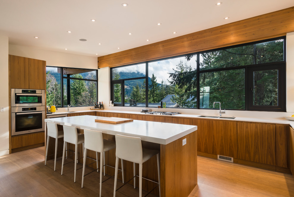 Medium sized contemporary u-shaped kitchen/diner in Vancouver with flat-panel cabinets, medium wood cabinets, engineered stone countertops, white splashback, window splashback, an island, brown floors, white worktops, a double-bowl sink, stainless steel appliances and medium hardwood flooring.