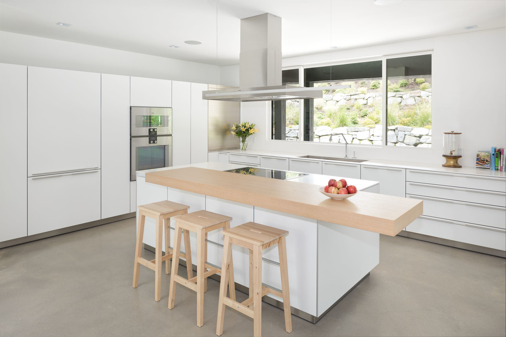 Idéer för minimalistiska kök, med en undermonterad diskho, släta luckor, vita skåp, fönster som stänkskydd, rostfria vitvaror, betonggolv, en köksö och grått golv