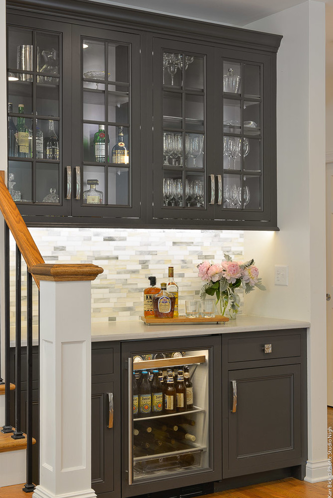 Example of a large transitional u-shaped medium tone wood floor and brown floor home bar design in Other with flat-panel cabinets, white cabinets, quartz countertops, white backsplash and porcelain backsplash