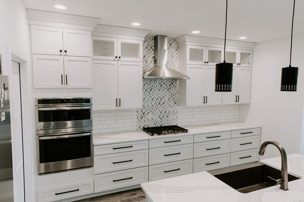 Example of a mid-sized transitional open concept kitchen design in Cedar Rapids with a farmhouse sink, shaker cabinets, white cabinets, quartz countertops, white backsplash, subway tile backsplash, stainless steel appliances, an island and white countertops