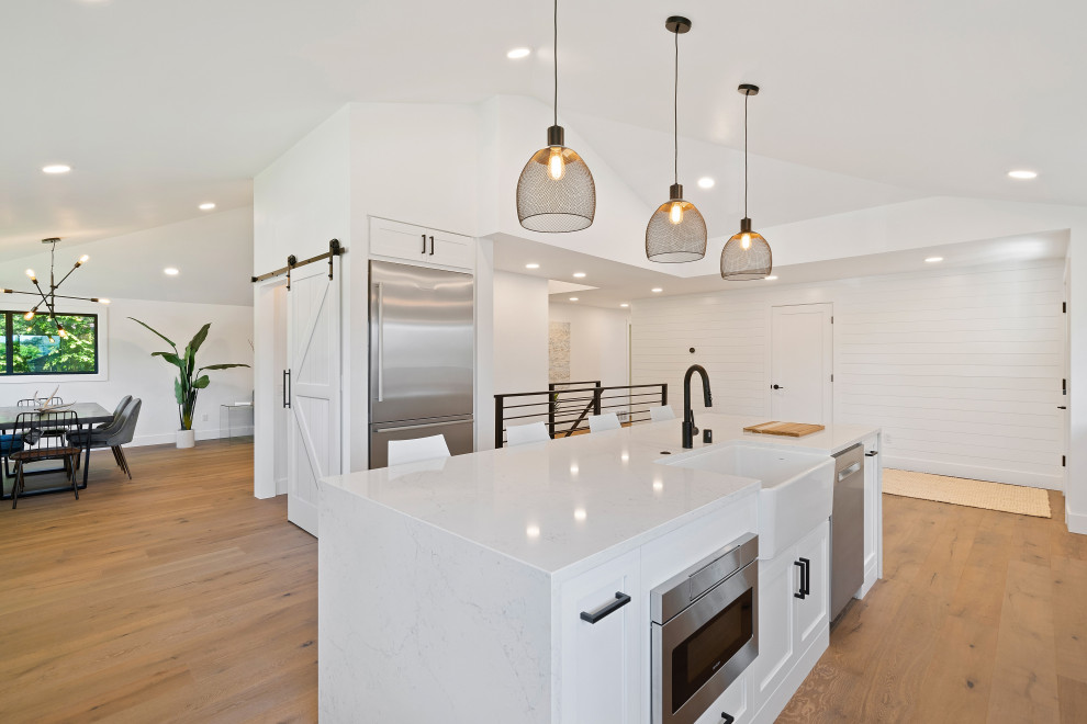 Imagen de cocina de estilo de casa de campo grande con fregadero sobremueble, encimera de mármol, salpicadero blanco, electrodomésticos de acero inoxidable, suelo de madera en tonos medios, una isla, suelo marrón y encimeras blancas