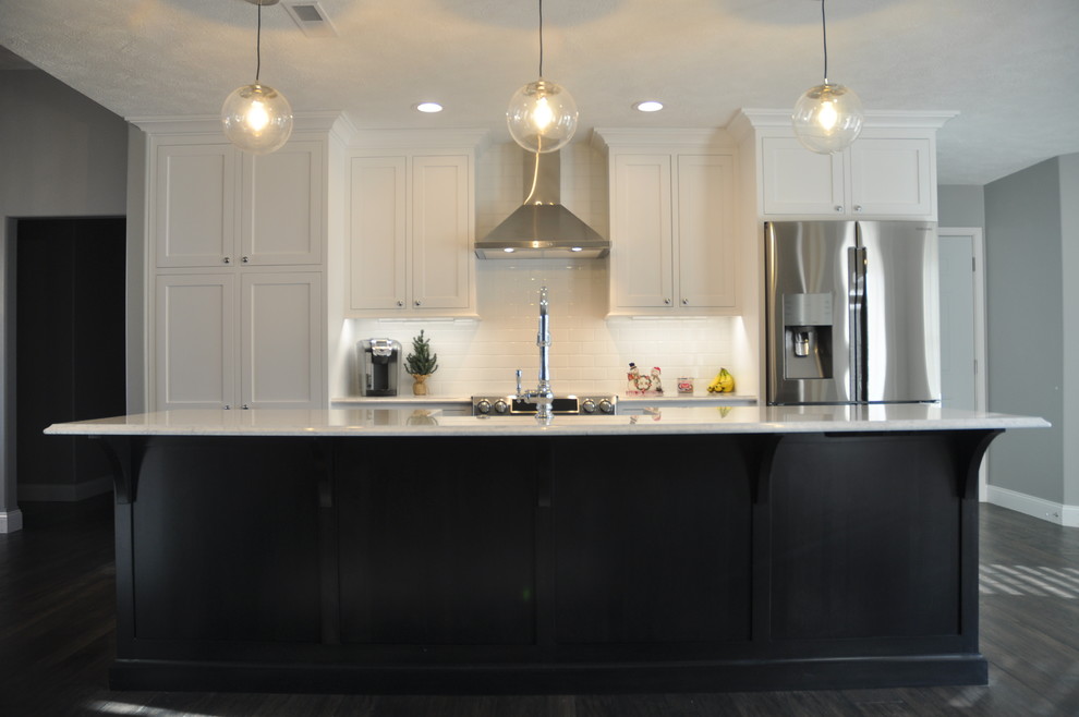 This is an example of a medium sized traditional single-wall kitchen/diner in St Louis with a belfast sink, recessed-panel cabinets, white cabinets, engineered stone countertops, white splashback, metro tiled splashback, stainless steel appliances, dark hardwood flooring, an island and brown floors.