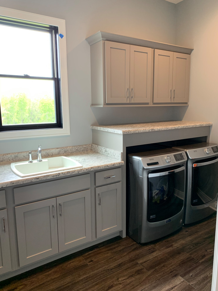 Laundry room - large farmhouse l-shaped vinyl floor and brown floor laundry room idea in Other with a farmhouse sink, flat-panel cabinets, gray cabinets, quartz countertops, metallic backsplash, metal backsplash and white countertops