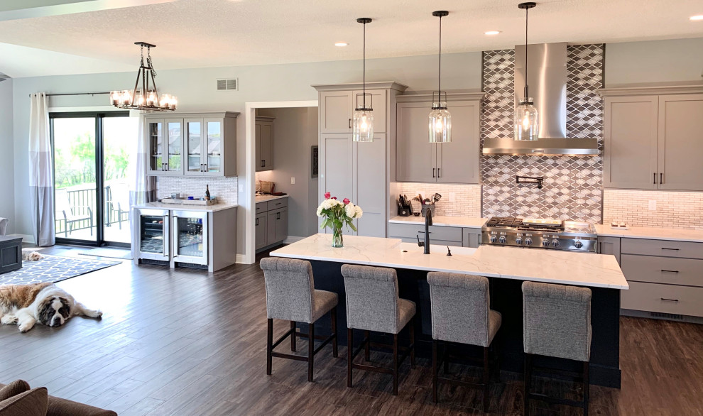 Example of a large cottage l-shaped vinyl floor and brown floor open concept kitchen design in Other with a farmhouse sink, flat-panel cabinets, gray cabinets, quartz countertops, metallic backsplash, metal backsplash, stainless steel appliances, an island and white countertops