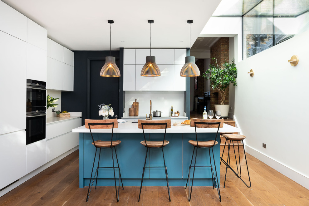 Design ideas for a contemporary l-shaped kitchen in London with a submerged sink, flat-panel cabinets, white cabinets, black appliances, medium hardwood flooring, an island, brown floors and white worktops.