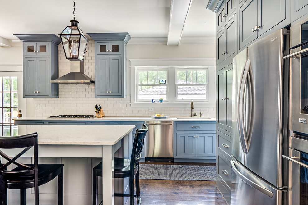 Exempel på ett stort klassiskt kök, med en undermonterad diskho, luckor med infälld panel, blå skåp, marmorbänkskiva, vitt stänkskydd, stänkskydd i keramik, rostfria vitvaror, mörkt trägolv och en köksö
