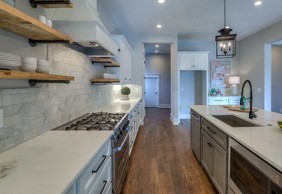 Foto på ett mellanstort amerikanskt vit linjärt kök med öppen planlösning, med en undermonterad diskho, luckor med infälld panel, vita skåp, granitbänkskiva, vitt stänkskydd, stänkskydd i keramik, rostfria vitvaror, mellanmörkt trägolv, en köksö och brunt golv