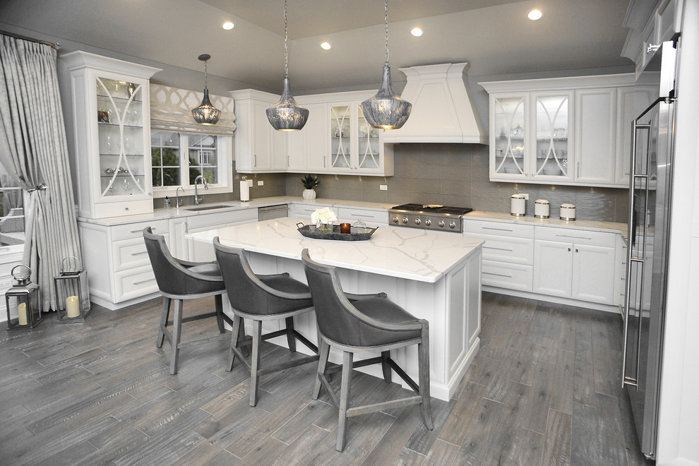 Photo of a large traditional u-shaped kitchen/diner in Chicago with a submerged sink, recessed-panel cabinets, white cabinets, quartz worktops, grey splashback, stainless steel appliances, laminate floors, an island, grey floors and white worktops.