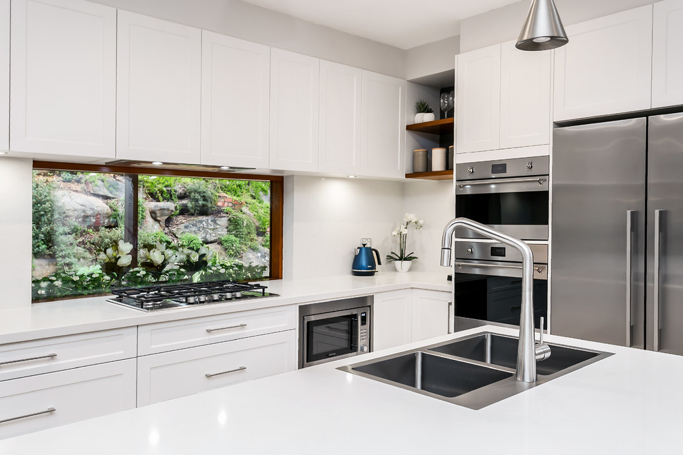 Design ideas for a large contemporary galley kitchen/diner with a double-bowl sink, shaker cabinets, white cabinets, engineered stone countertops, window splashback, stainless steel appliances, light hardwood flooring, an island, brown floors and white worktops.