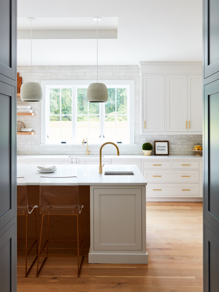 Inspiration for a large classic l-shaped kitchen in New York with a submerged sink, shaker cabinets, white cabinets, engineered stone countertops, grey splashback, ceramic splashback, medium hardwood flooring, an island, beige floors and white worktops.