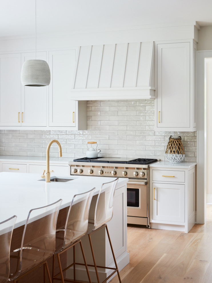 This is an example of a large traditional l-shaped kitchen in New York with a submerged sink, shaker cabinets, white cabinets, engineered stone countertops, grey splashback, ceramic splashback, stainless steel appliances, medium hardwood flooring, an island, beige floors and white worktops.