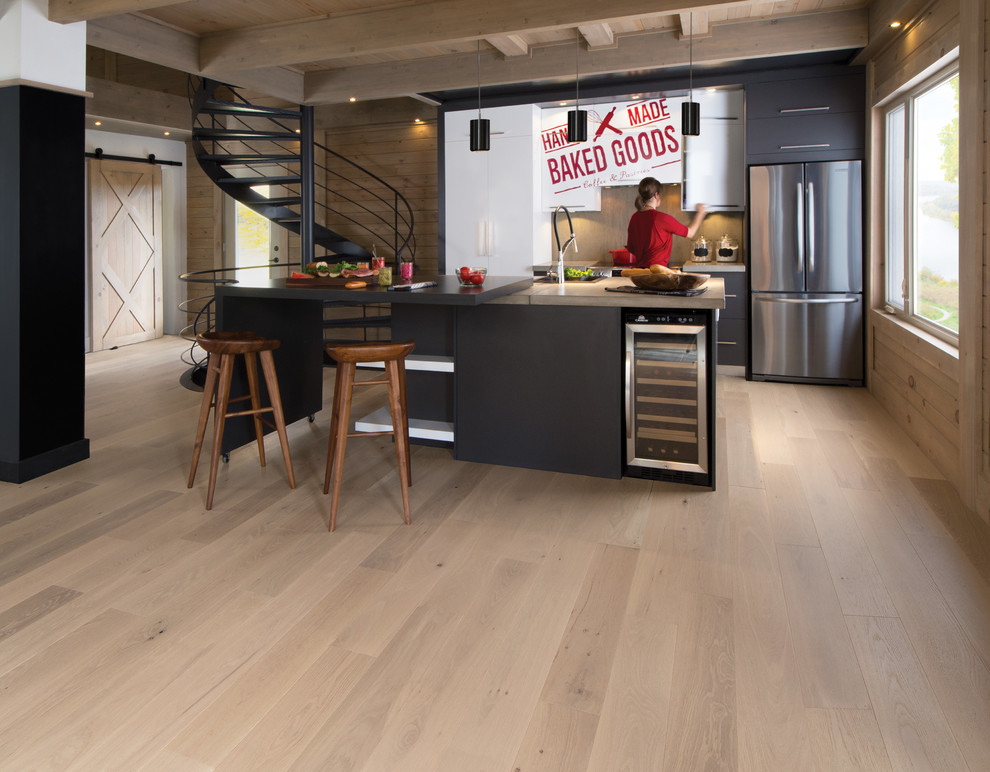 Photo of a small modern galley kitchen/diner in Los Angeles with flat-panel cabinets, black cabinets, concrete worktops, grey splashback, stainless steel appliances, light hardwood flooring, an island, beige floors and grey worktops.