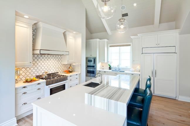 Klassisk inredning av ett mellanstort kök, med en dubbel diskho, skåp i shakerstil, vita skåp, marmorbänkskiva, vitt stänkskydd, stänkskydd i mosaik, integrerade vitvaror, ljust trägolv och en köksö