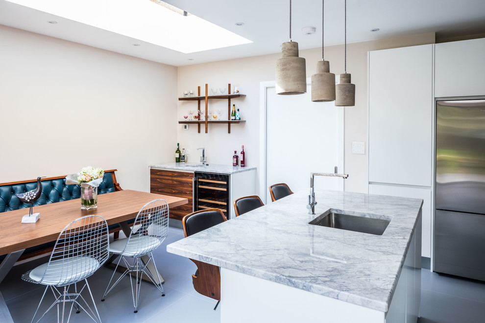 Medium sized contemporary l-shaped open plan kitchen in Oxfordshire with flat-panel cabinets, white cabinets, grey floors, stainless steel appliances, a single-bowl sink, granite worktops, metallic splashback, ceramic flooring and a breakfast bar.