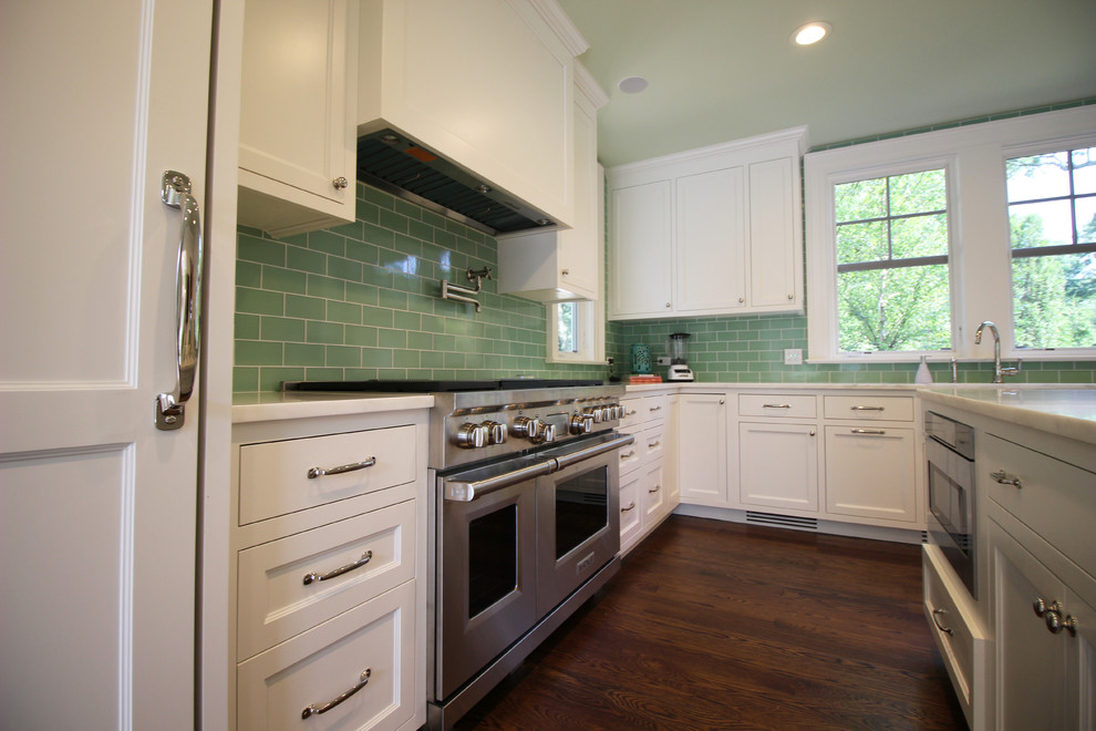 Klassisk inredning av ett avskilt, stort l-kök, med en rustik diskho, luckor med infälld panel, vita skåp, marmorbänkskiva, grönt stänkskydd, stänkskydd i tunnelbanekakel, rostfria vitvaror, mellanmörkt trägolv och en köksö