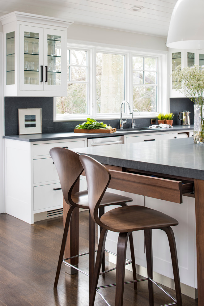 Inspiration for a large transitional l-shaped medium tone wood floor eat-in kitchen remodel in New York with a single-bowl sink, shaker cabinets, white cabinets, limestone countertops, gray backsplash, stone slab backsplash, stainless steel appliances and an island