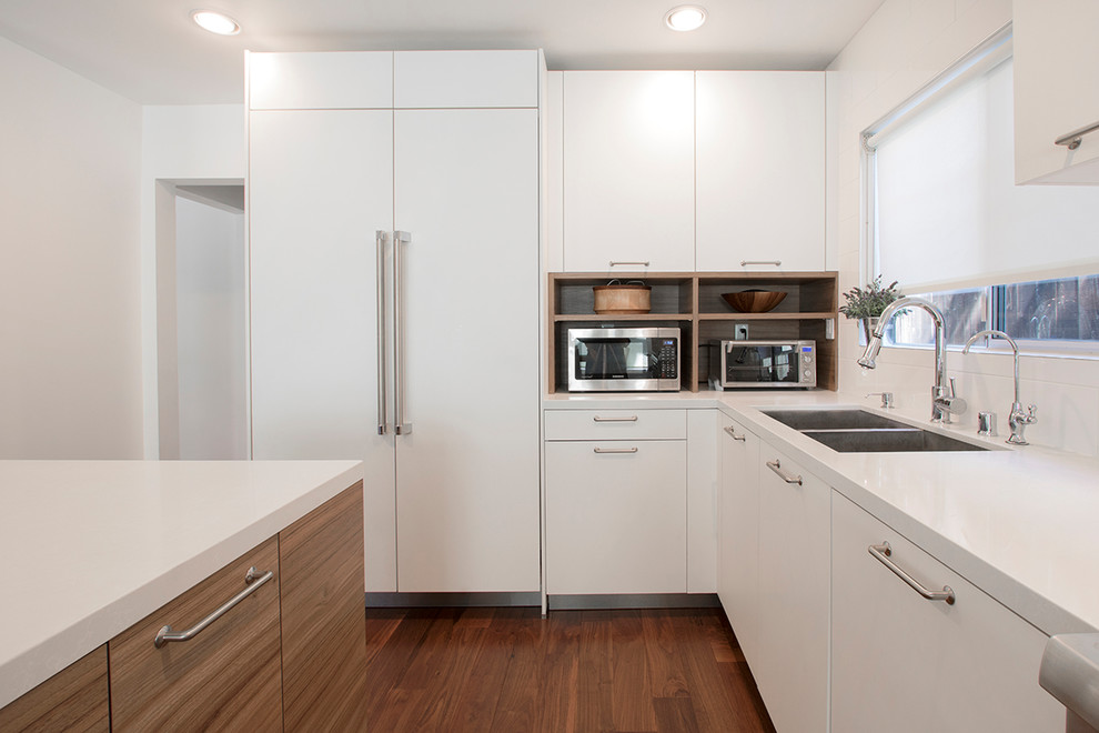 Idéer för att renovera ett mellanstort funkis vit vitt kök, med en nedsänkt diskho, släta luckor, skåp i mellenmörkt trä, bänkskiva i kvartsit, vitt stänkskydd, stänkskydd i porslinskakel, rostfria vitvaror, laminatgolv, en köksö och brunt golv