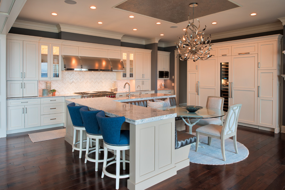 Open concept kitchen - large traditional l-shaped dark wood floor and brown floor open concept kitchen idea in Minneapolis with a farmhouse sink, recessed-panel cabinets, beige cabinets, white backsplash, ceramic backsplash, stainless steel appliances, an island and white countertops